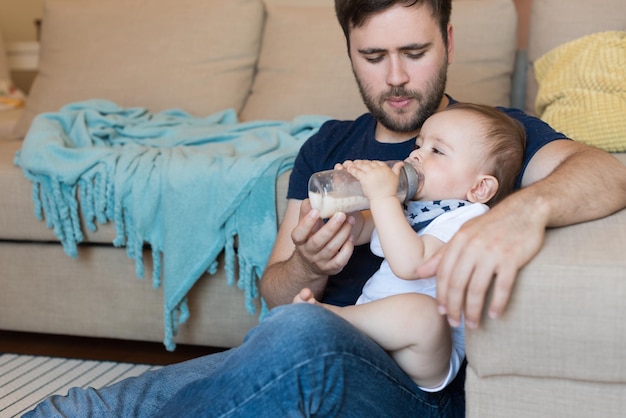 Junger Vater, der sein Baby mit Säuglingsflasche füttert