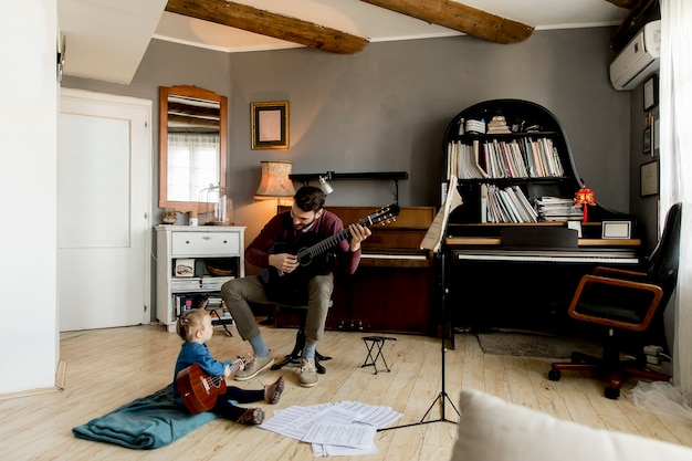 Junger Vater und kleine Tochter, die zu Hause Akustikgitarre im Raum spielt