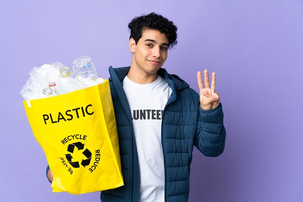Junger venezolanischer Mann, der eine Tasche voller Plastikflaschen glücklich hält und drei mit den Fingern zählt