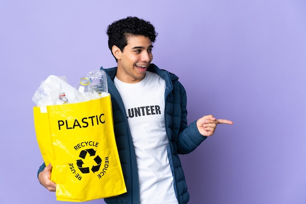 Junger venezolanischer Mann, der eine Tasche voller Plastikflaschen hält, die Finger zur Seite zeigen und ein Produkt präsentieren