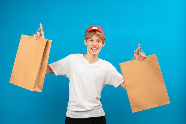 Junger Verkäufer in lässigem weißem T-Shirt mit Papiertüte isoliert auf blauem Hintergrund Studioporträt People Lifestyle-Konzept Mock-up-Kopierbereich Teen holding Paketbeutel mit Einkäufen