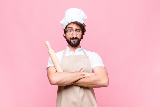 Junger verrückter Bäcker mit einem Kochwerkzeug gegen rosa Wand