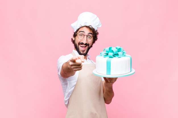 Junger verrückter Bäckermann, der einen Kuchen gegen rosa Wand hält