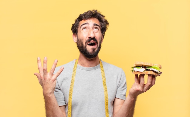 Junger verrückter bärtiger Mann, der traurigen Ausdruck nährt und ein Sandwich hält