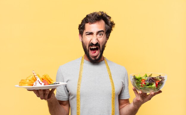 Junger verrückter bärtiger Mann mit wütendem Ausdruck und hält einen Salat und Waffeln?