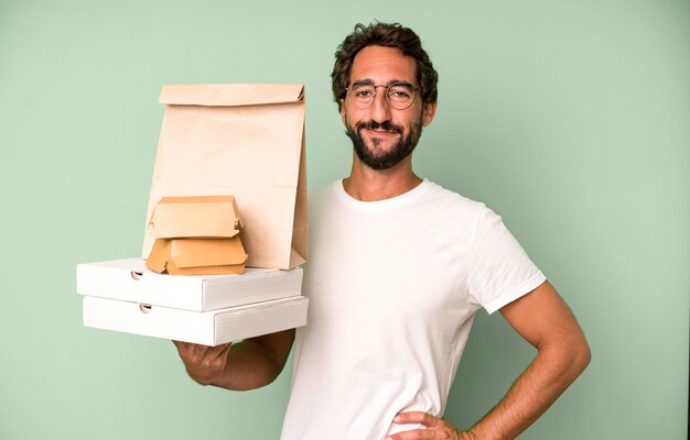 Foto junger verrückter bärtiger und ausdrucksstarker mann, der fast-food-leere leere verpackungen mitnimmt