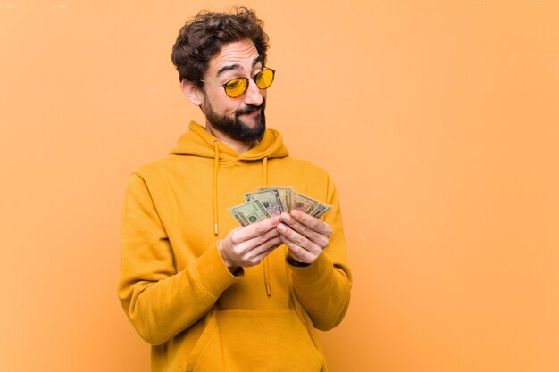 Junger verrückter cooler Mann mit Dollarbanknoten auf orange Wand