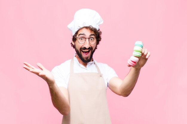 Junger verrückter cooler Mann mit Macarons auf rosa Wand