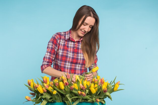 Junger weiblicher Florist mit großer Schachtel der gelben Tulpen auf blauer Oberfläche