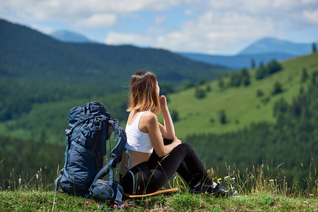 Junger weiblicher Rucksacktourist mit blauem Rucksack, der oben auf einem Hügel sitzt