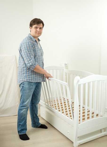 Junger werdender Vater, der Bett für sein zukünftiges Baby zusammenbaut