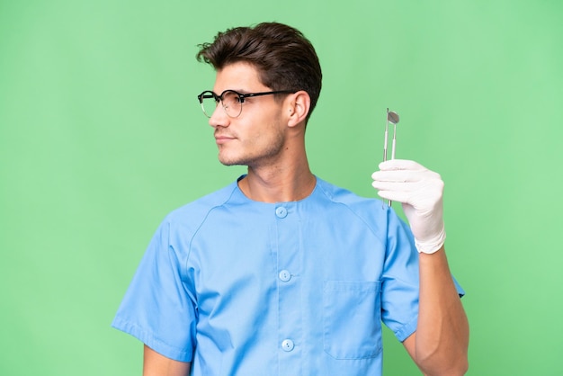 Junger Zahnarzt, der Werkzeuge über isoliertem Hintergrund hält und zur Seite schaut