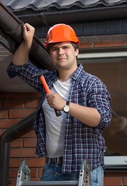 Junger Zimmermann im Bauarbeiterhelm, der Hausdach untersucht