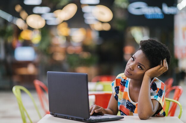 Junges Afroamerikanermädchen, das am Kaffeetisch mit Laptop sitzt und Bildschirm betrachtet. Dunkelhäutiges Freiberuflerkonzept.