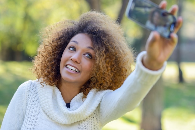 Junges Afroamerikanermädchen selfie im Park mit einem Smartphone