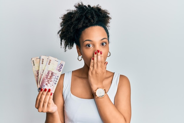 Foto junges afroamerikanisches mädchen, das 500 neue taiwan-dollar-banknoten in der hand hält und den mund mit der hand bedeckt, ist schockiert und hat angst vor einem fehler und hat einen überraschten gesichtsausdruck