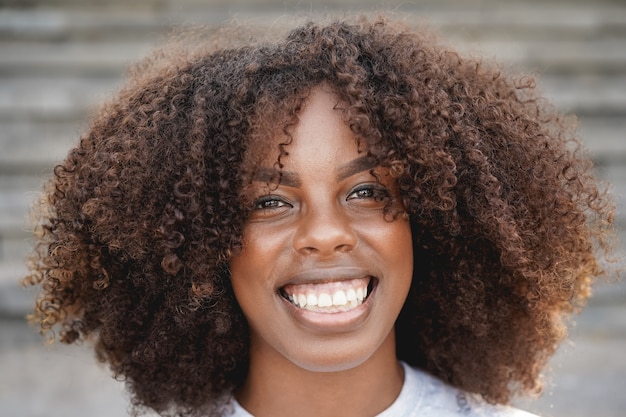 Junges afroamerikanisches Mädchen, das auf der Kamera im Freien in der Stadt lächelt - Fokus auf Gesicht