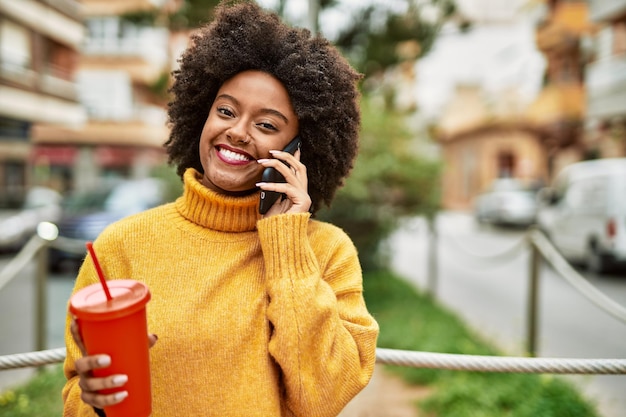 Junges afroamerikanisches Mädchen, das in der Stadt auf dem Smartphone spricht und Limonade trinkt