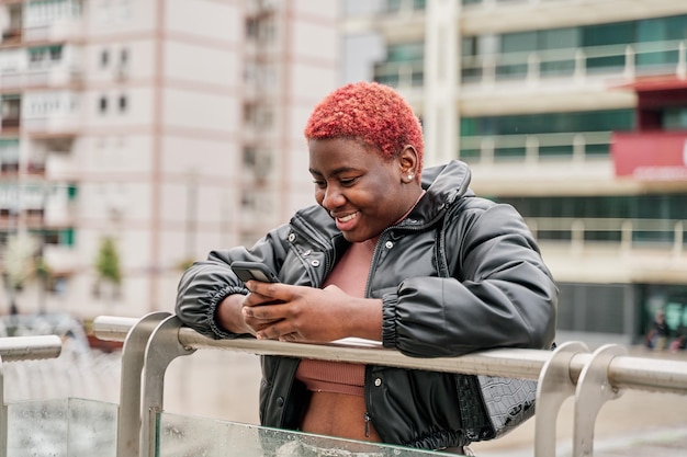 Junges afroamerikanisches Mädchen, das mit ihrem Handy in der Stadt lächelt