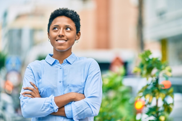 Junges afroamerikanisches Mädchen mit verschränkten Armen lächelt glücklich in die Stadt