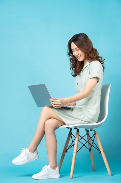 Junges asiatisches Mädchen, das auf einem Stuhl unter Verwendung eines Laptops mit einem glücklichen Ausdruck sitzt