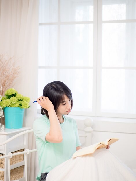 Junges asiatisches Mädchen, das ein Buch im Bett liest