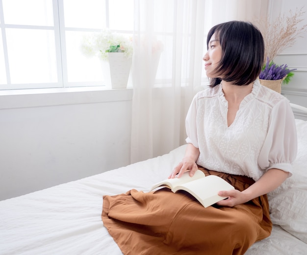 Junges asiatisches Mädchen, das ein Buch im Bett liest