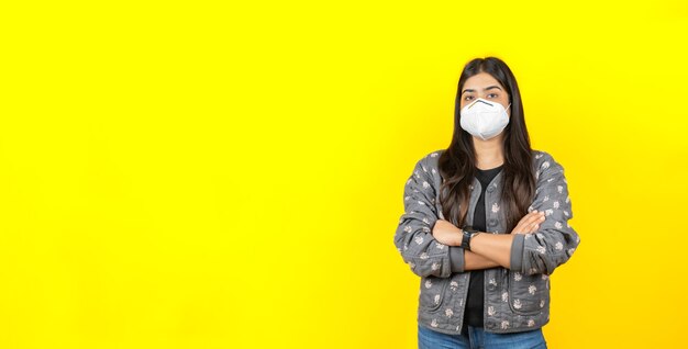 Junges asiatisches Mädchen, das eine medizinische Gesichtsmaske in Freizeitkleidung trägt, isoliert auf gelbem Hintergrund