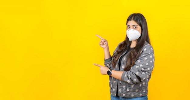 Junges asiatisches Mädchen, das eine medizinische Gesichtsmaske in Freizeitkleidung trägt, isoliert auf gelbem Hintergrund