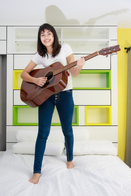 Junges asiatisches Mädchen, das Gitarre in ihrem Schlafzimmer spielt?