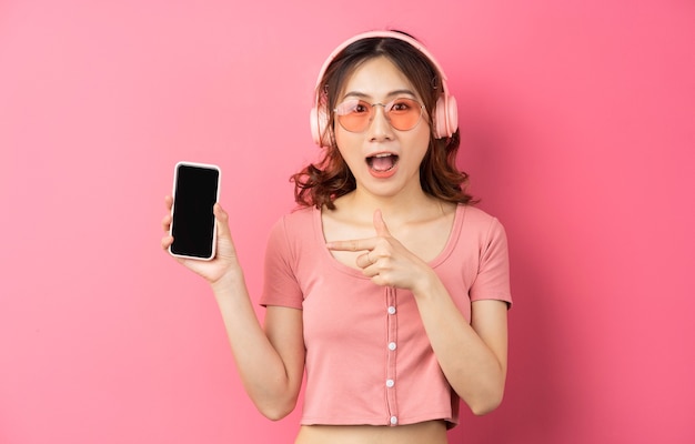 Junges asiatisches Mädchen, das Kopfhörer trägt und das Telefon auf Rosa benutzt
