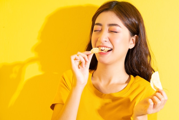 Junges asiatisches Mädchen, das Snack auf Gelb isst