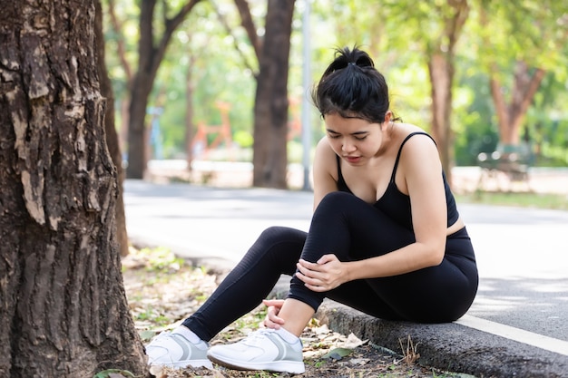 Junges asiatisches Mädchen in Sportbekleidung, die ihre Muskeln Knöchel schmerzhafte Verletzung außerhalb nach dem Training in der Naturstraße berührt. Sportverletzungskonzept.