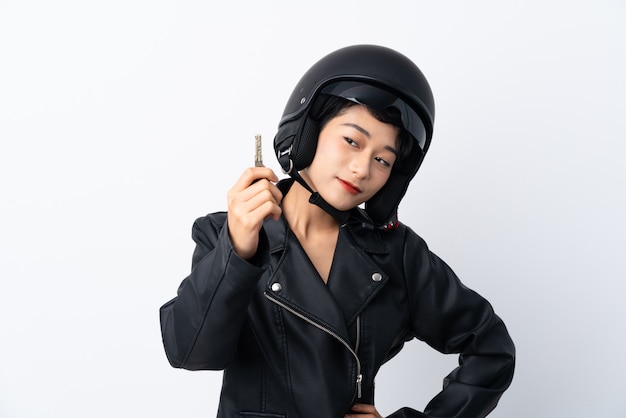 Junges asiatisches Mädchen mit einem Motorradsturzhelm und einem Schlüssel über lokalisierter weißer Wand