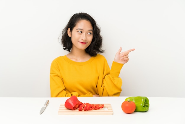 Junges asiatisches Mädchen mit Gemüse in einer Tabelle Finger auf die Seite zeigend