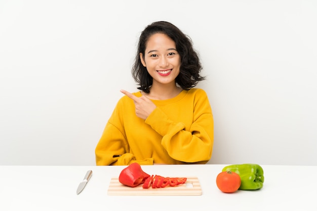 Junges asiatisches Mädchen mit Gemüse in einer Tabelle Finger auf die Seite zeigend