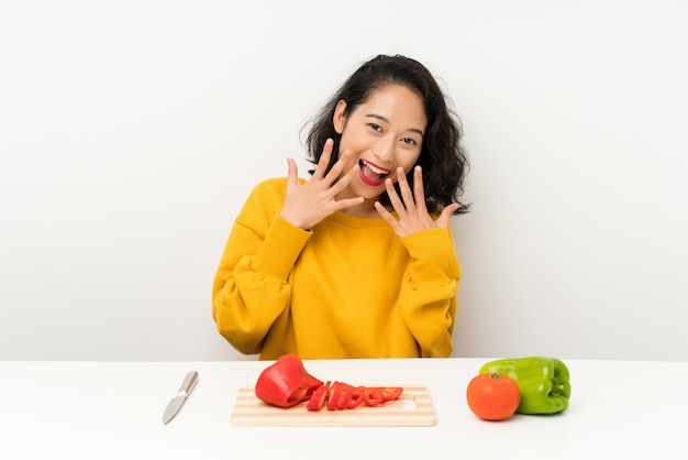 Junges asiatisches Mädchen mit Gemüse in einer Tabelle mit Überraschungsgesichtsausdruck