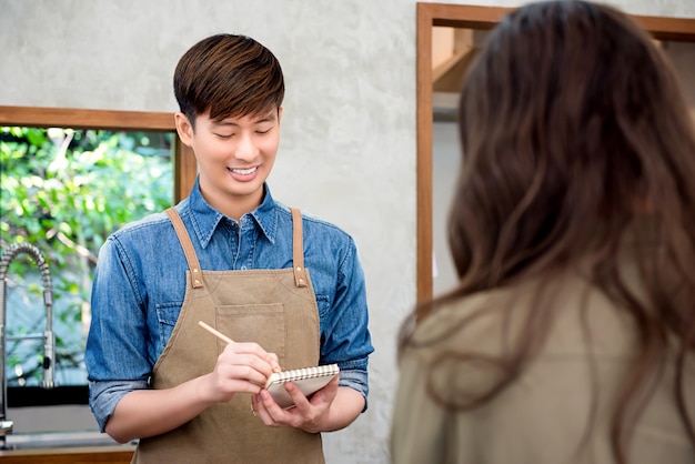 Junges asiatisches Mannkaffeestubepersonal, das Bestellung vom Kunden entgegennimmt