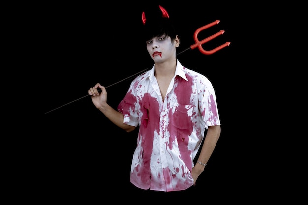 Junges asiatisches Mannkostüm in der Hölle, böse auf schwarzer Wand mit Konzept für Halloween-Modefestival. Teen asiatischer Mann im Cosplay Halloween.
