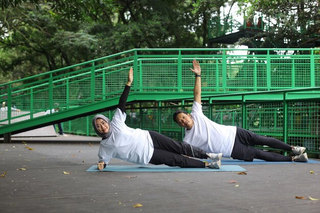 Junges asiatisches muslimisches Paar, das im Park zusammen Seitenplanken macht. Mann und Frau trainieren zusammen