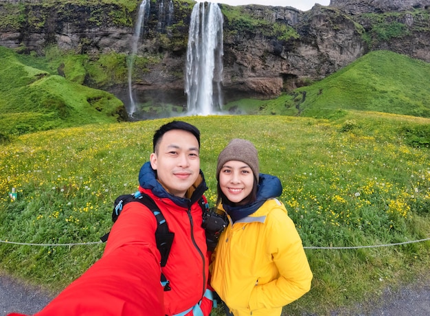 Junges asiatisches Paar touristisches Selfie mit Kamera am berühmten Ort des Wasserfalls im Sommer