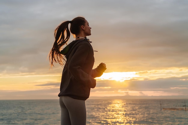 Junges athletisches langhaariges Mädchen, das bei Sonnenuntergang am Meer joggt, will abnehmen