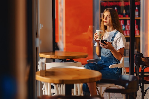 Junges attraktives hübsches Mädchen am Café mit Kaffee und Telefon am Morgen strahlt