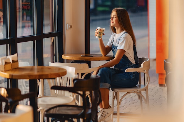 Junges attraktives hübsches Mädchen am Café mit Kaffee und Telefon am Morgen strahlt