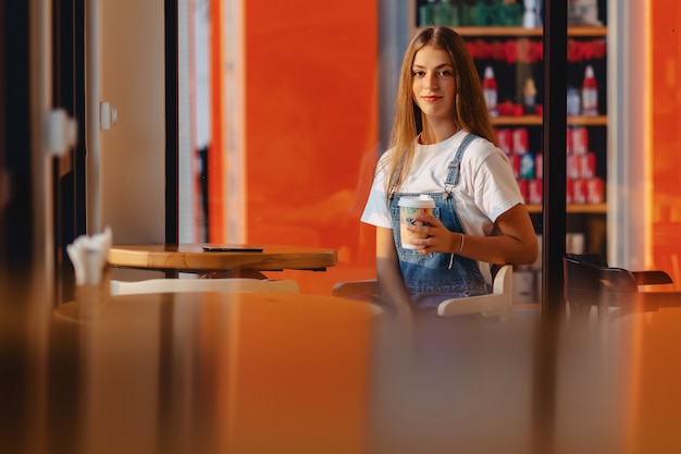 Junges attraktives hübsches Mädchen am Café mit Kaffee und Telefon am Morgen strahlt