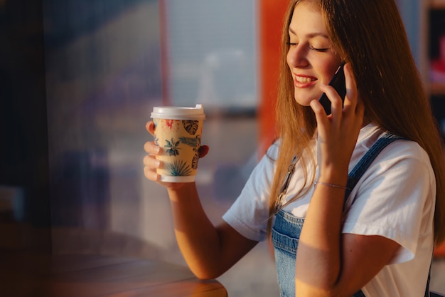 Junges attraktives hübsches Mädchen am Café mit Kaffee und Telefon am Morgen strahlt