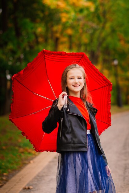Junges attraktives lächelndes Mädchen unter Regenschirm in einem Herbstwald