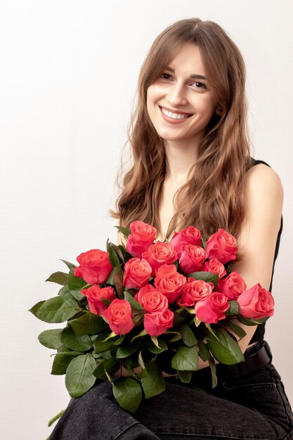 Junges attraktives Mädchen mit einem Strauß roter Rosen auf weißem Hintergrund Ein glückliches Mädchen mit einem Strauß Rosen lächelt Das Konzept von Glück, Freude und Feier