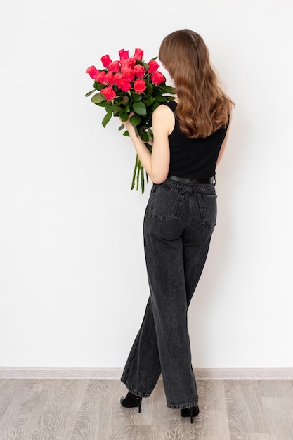 Junges attraktives Mädchen mit einem Strauß roter Rosen in vollem Wachstum auf weißem Hintergrund Rückansicht Das Konzept von Glück, Freude und Feier