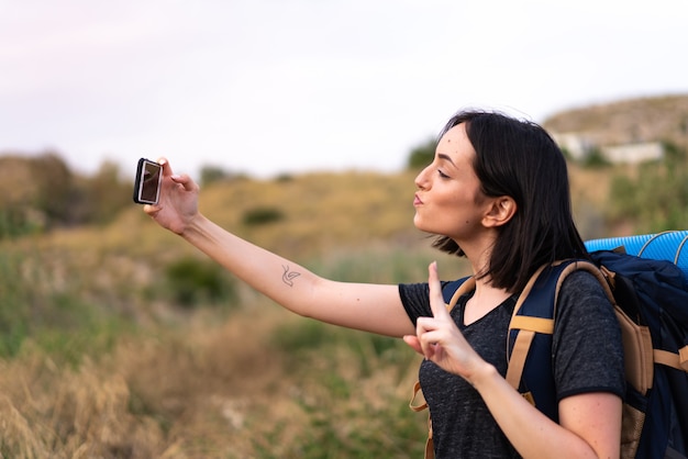 Junges Bergsteigermädchen, das ein Selfie mit dem Handy mit einem großen Rucksack im Freien nimmt